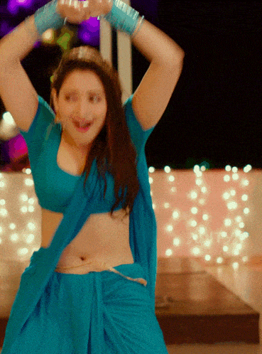 a woman in a blue top and skirt is dancing with her arms in the air