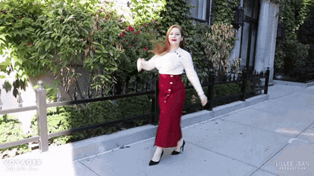 a woman is walking down a sidewalk wearing a red skirt and a white sweater .