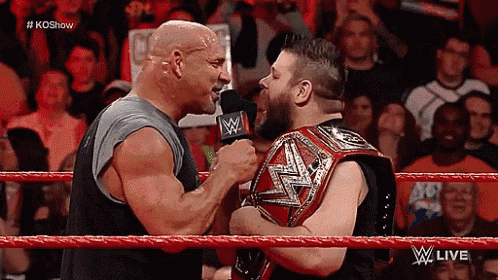 two wrestlers are talking to each other in a wrestling ring with a crowd watching .