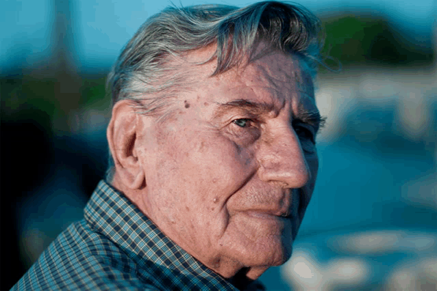 a man with gray hair and a plaid shirt looks to the side