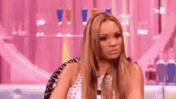 a woman is sitting in a chair in front of a pink wall and making a funny face .