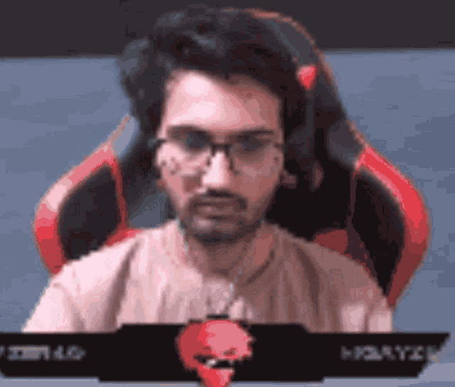 a man with glasses and a beard is sitting in a red chair .