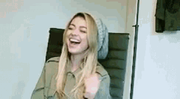 a woman is sitting in a chair laughing while wearing a beanie .