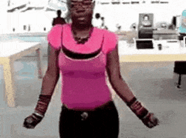 a woman in a pink shirt and black pants is dancing in a room with her arms outstretched .