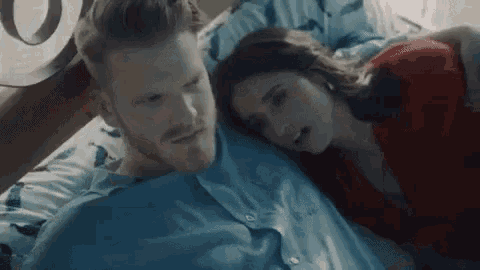 a man and a woman are laying on a bed and the woman is yawning