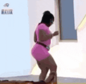a woman in a pink dress is dancing in front of a window in a room .