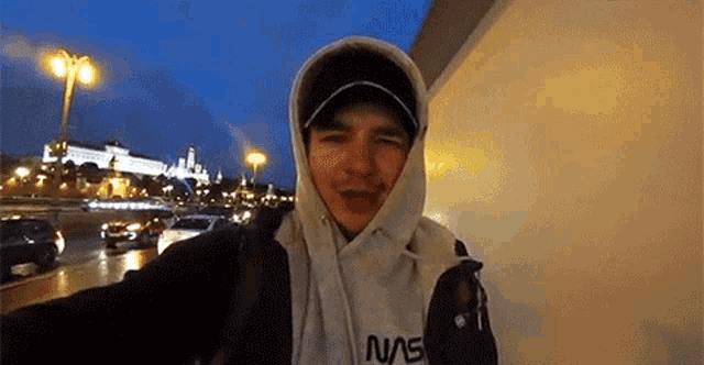 a man wearing a nasa hoodie is taking a selfie in front of a building .