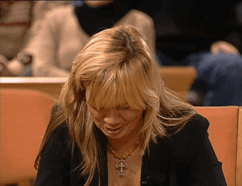 a woman wearing a black jacket and a gold cross necklace is smiling