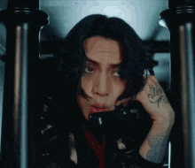 a man with long black hair and a tattoo on his arm is sitting in a chair talking on a phone .
