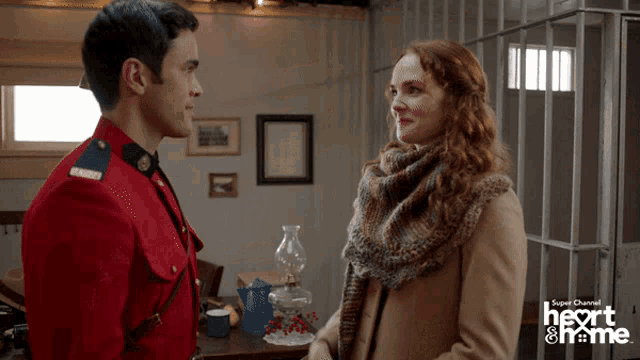 a man in a red uniform stands next to a woman in a brown coat and the words heart & home are on the bottom