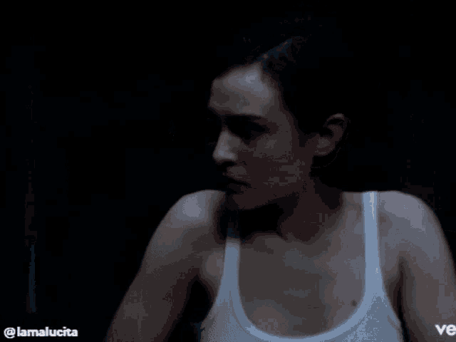 a woman in a white tank top is looking at the camera