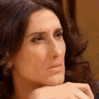 a woman is sitting on a couch with her hand on her chin and looking at the camera .