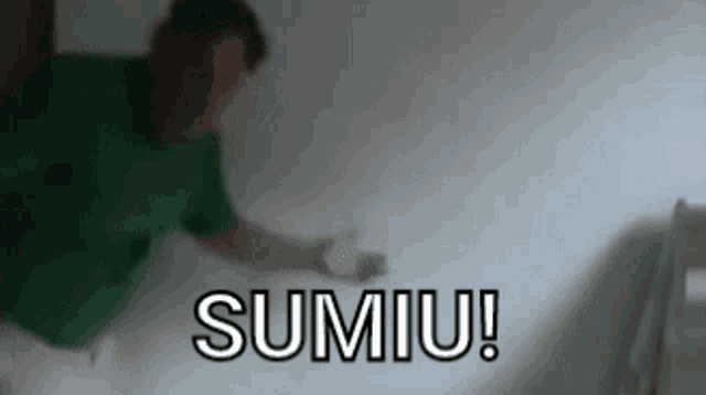 a man in a green shirt is standing in front of a white wall with the word sumiu written on it .