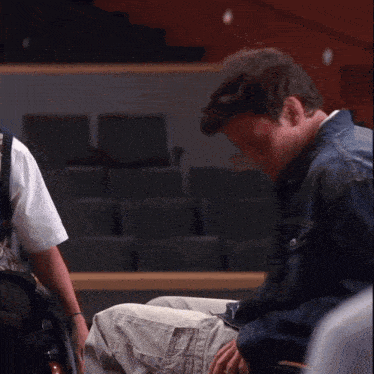 a man in a denim jacket is kneeling down in front of a man in a wheelchair