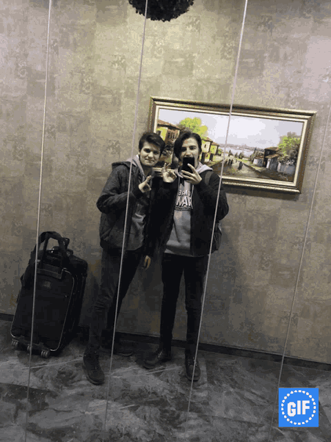 two boys are taking a picture of themselves in front of a painting that says gif on the bottom
