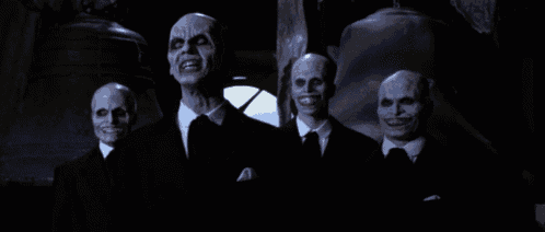 a group of bald men in suits and ties are standing in the dark