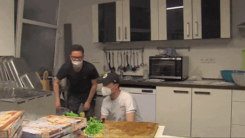 a man wearing a mask is standing in a kitchen next to another man