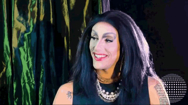 a drag queen with a tattoo on her arm smiles
