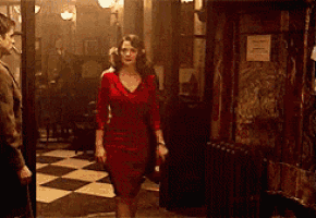 a woman in a red dress is walking down a checkered floor in a room .