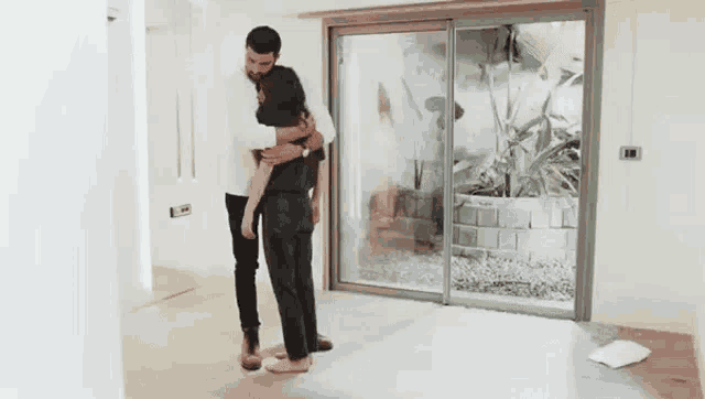 a man and a woman are hugging in an empty room in a house .