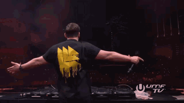 a man in a black shirt with a yellow triangle on the back is dancing in front of a screen that says uhf tv