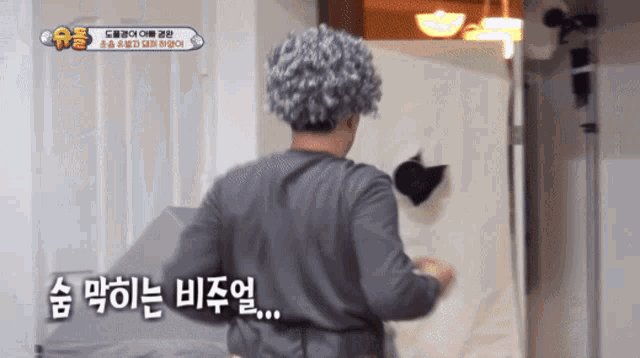 a man wearing a gray wig stands in front of a white wall with korean writing on it