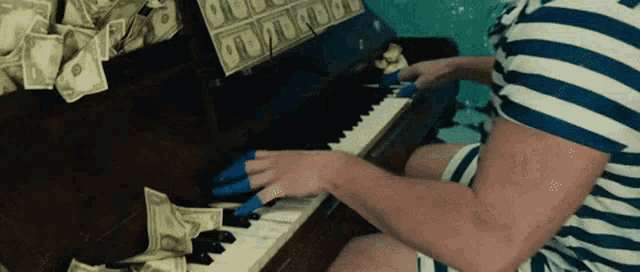 a man in a striped shirt is playing a piano with money on the keys