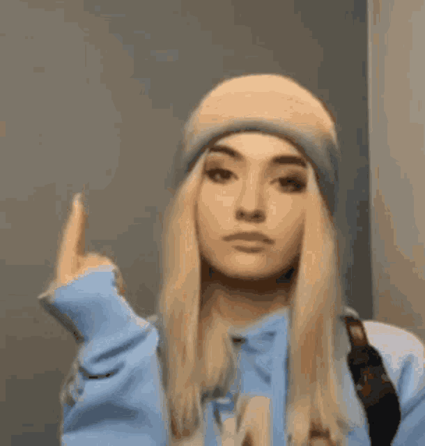 a blonde woman wearing a blue hoodie and a beanie is giving the middle finger .
