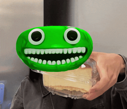a person holding a container of cheesecake with a green face on it