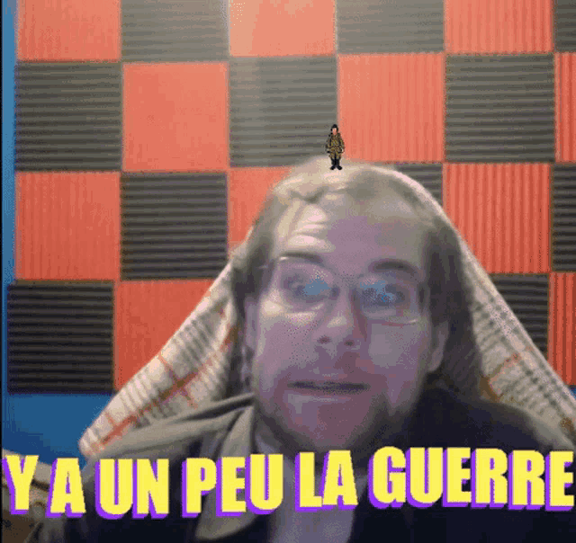 a man with glasses is sitting in front of a wall that says ya un peu la guerre on it