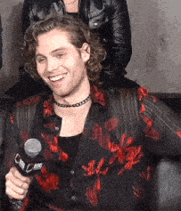a man with curly hair is holding a microphone and smiling while wearing a choker .