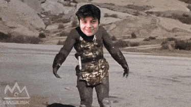 a young boy in a costume is standing in the sand with a basilisk logo behind him