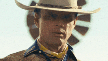a man wearing a cowboy hat is standing in front of a windmill and a fallout logo