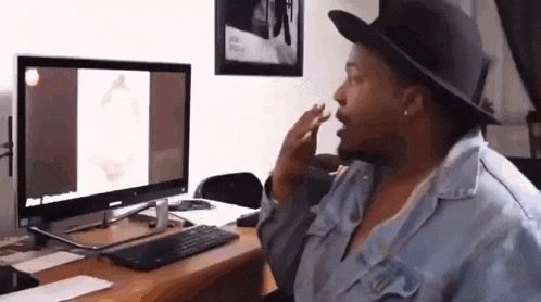 a woman wearing a hat is sitting in front of a computer screen .