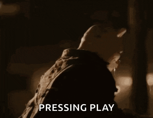 a man is standing in a dark room with the words `` pressing play '' written on the screen .