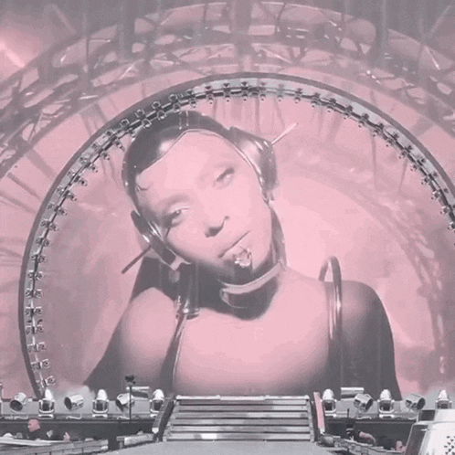 a woman wearing headphones stands in front of a pink arch