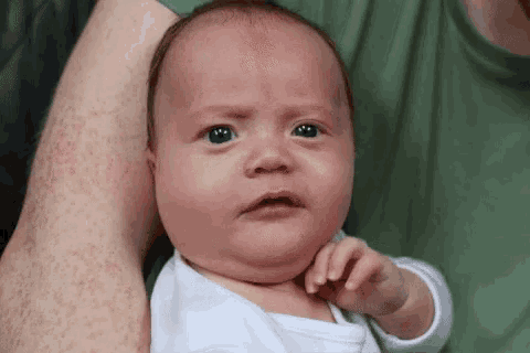 a baby is being held by a man in his arms and making a funny face .