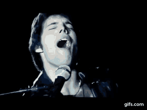 a man is singing into a microphone with his mouth open in the dark .