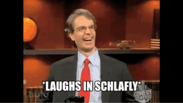 a man in a suit and tie is laughing while sitting on a stage .
