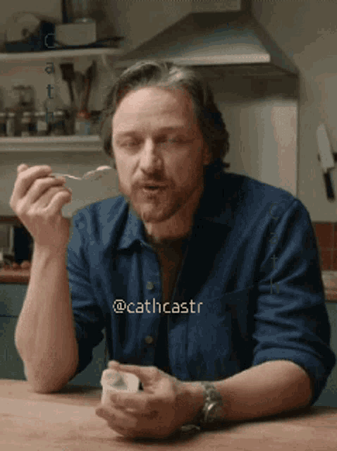 a man in a blue shirt is sitting at a table eating something with a spoon