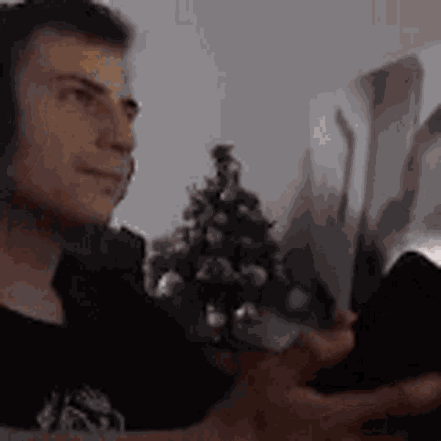 a man is sitting in front of a christmas tree and looking at a picture .