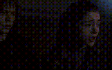 a woman is covering her mouth with her hand while looking at a cell phone in the dark .