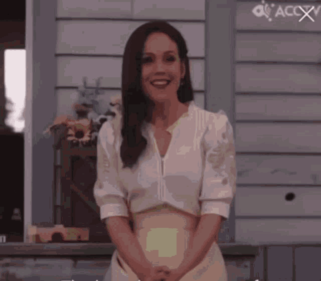 a woman in a white dress is standing in front of a building and smiling