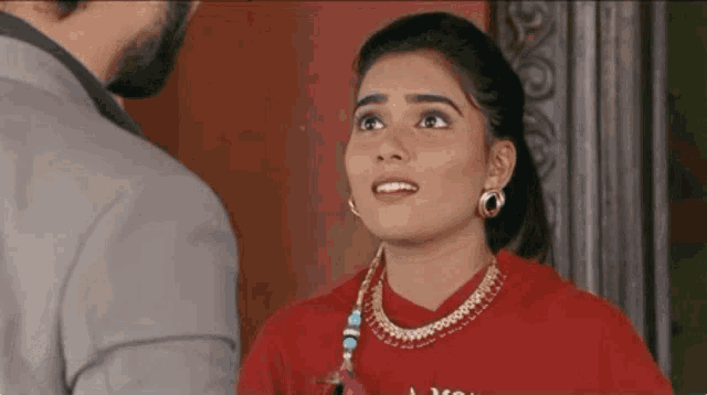 a man and a woman are standing next to each other and the woman is wearing a red shirt and earrings .