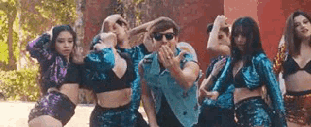 a man wearing sunglasses is standing in front of a group of women .