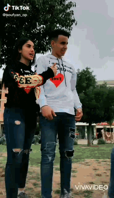 a man and a woman are standing next to each other in a park with trees in the background