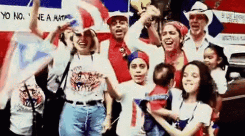 a group of people are standing in front of a car holding flags and a baby .