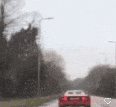 a red car is driving down a road with a heart in the middle