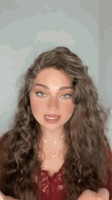 a woman with long curly hair wearing a red top