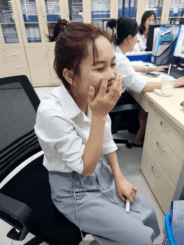 a woman sitting in a chair covering her mouth with her hands